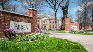Photo of Berea College campus with Berea sign written on the left of the walkway surrounded by greenery.