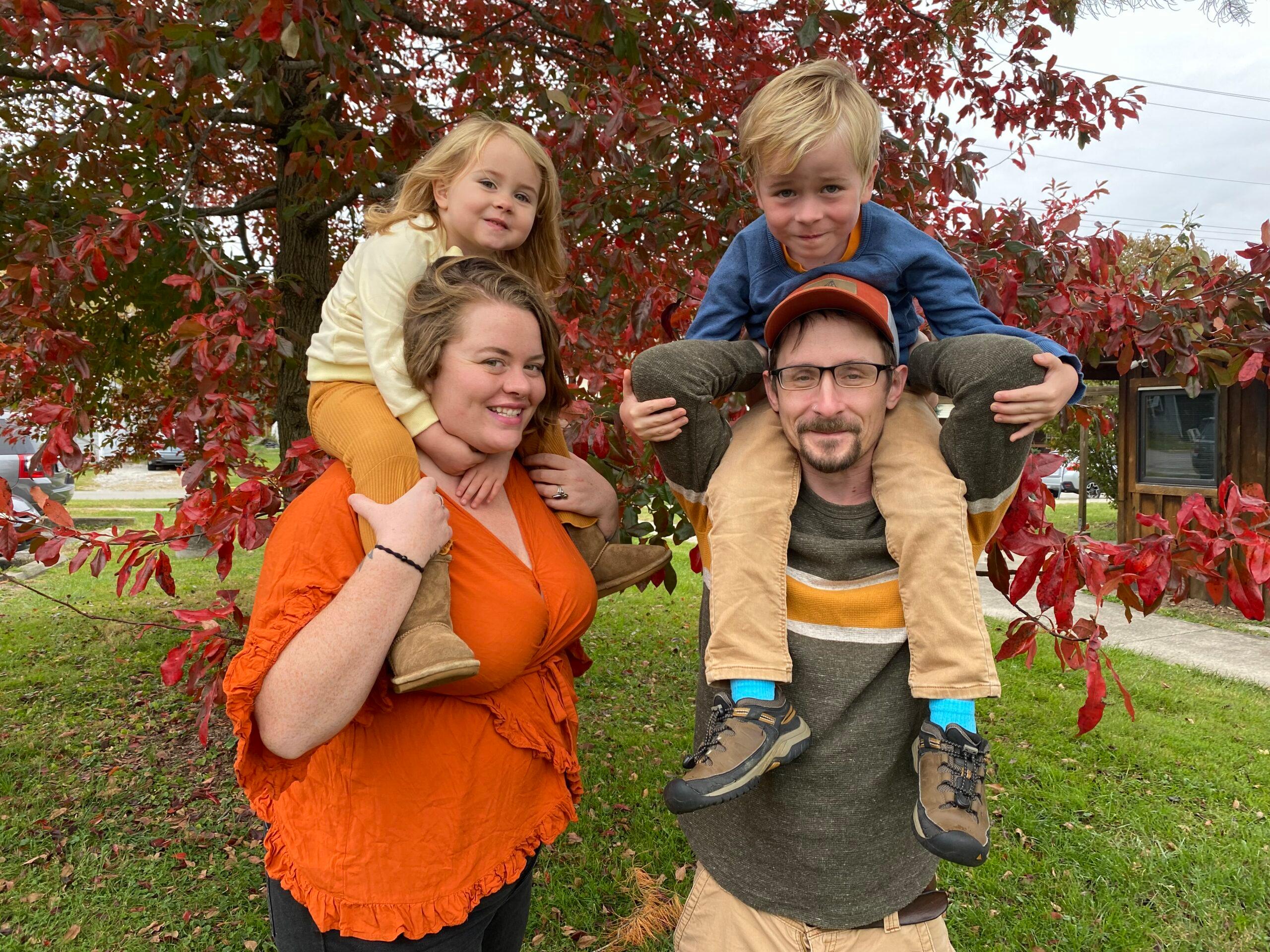 Liz and her husband standing with their two children sitting on their shoulders.