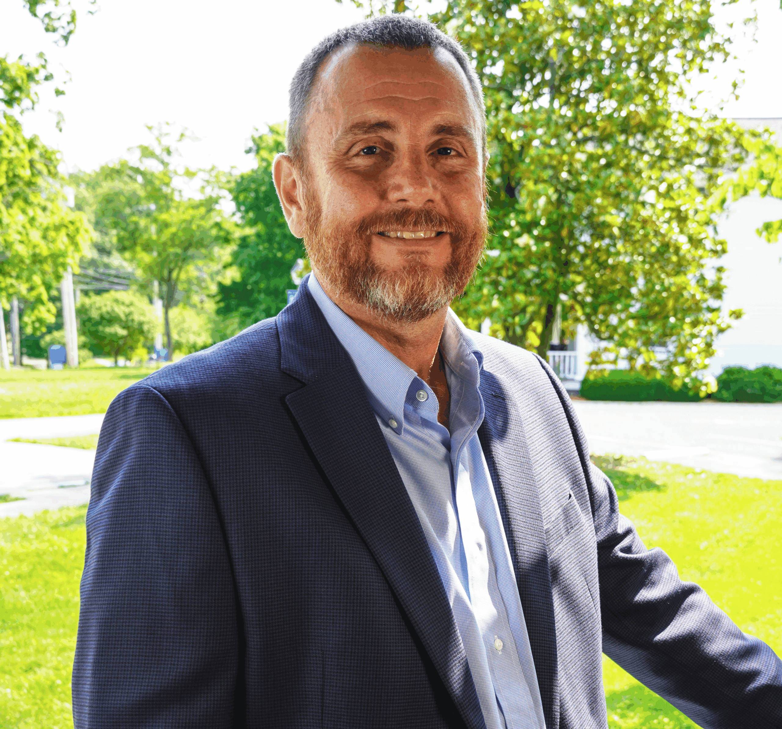 A photo of Regional Admissions Manager for the Eastern Kentucky region, David Gibson, standing outside amongst green grass and trees, wearing a blue collared shirt and navy blue blazer, smiling.