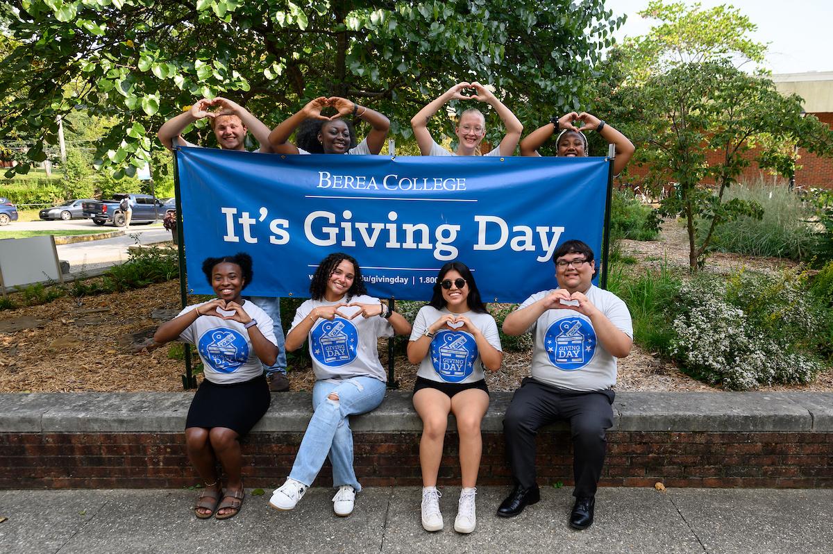 Students making heart hands with a Giving Day banner.